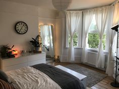 a bedroom with two windows and a large bed in front of the window is lit by candles