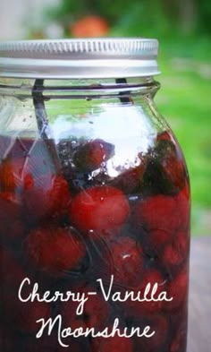 a mason jar filled with cherries sitting on top of a wooden table next to grass