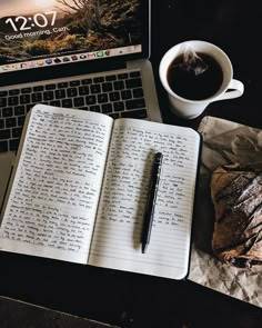 an open notebook sitting on top of a table next to a cup of coffee and a laptop