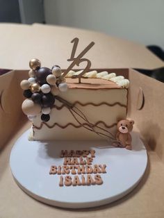 a birthday cake with balloons and a teddy bear on it's side sitting in a cardboard box