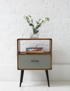 a white brick wall behind a nightstand with flowers in it