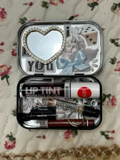 an open tin with various items in it sitting on a floral bed sheet, next to a mirror