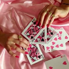 a woman's hands holding four playing cards on a pink satin sheeted surface