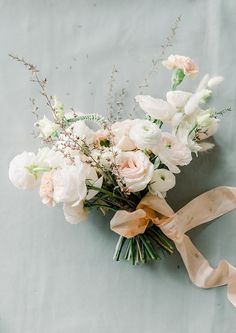 a bouquet of white and pink flowers on a gray surface with a ribbon tied around it