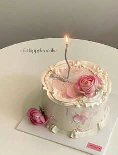 a birthday cake with a single lit candle on it and pink flowers in the middle