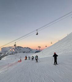 skiers and snowboarders at the bottom of a ski slope as the sun sets