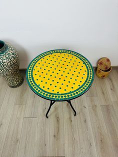 a yellow and green table sitting on top of a wooden floor next to two vases