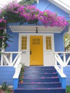 a blue house with purple flowers growing over the front door and steps leading up to it