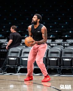 a man holding a basketball while standing on top of a basketball court with other men in the background