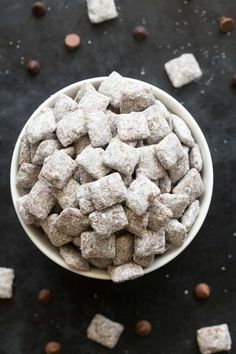 a white bowl filled with brown and white puppy chow next to chocolate chips on a black surface