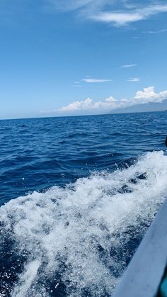 the back end of a boat traveling through the ocean on a sunny day with blue skies and clouds