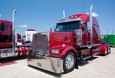 a red semi truck parked in a parking lot next to other trucks and trailer trailers