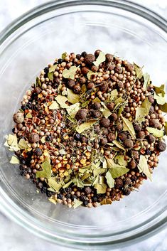 a glass bowl filled with lots of different types of spices and herbs on top of a marble surface