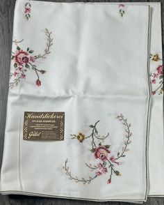 two white handkerchiefs with pink and yellow flowers are on a wooden table next to a brown label