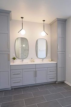 a bathroom with double sinks and two mirrors on the wall next to gray tile flooring