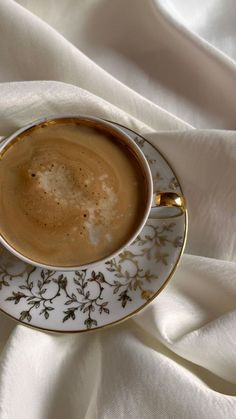 a cup of coffee sitting on top of a saucer covered in white and gold