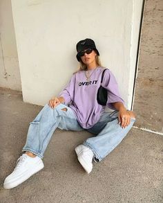 a woman sitting on the ground wearing a purple shirt and jeans with white converse shoes