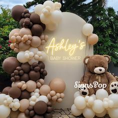 a teddy bear sitting in front of a baby shower sign with balloons all over it