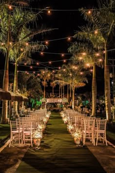 an outdoor wedding venue with white chairs and lights strung from the ceiling, surrounded by palm trees