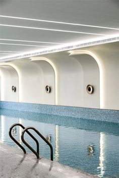 an indoor swimming pool with blue water and white walls, lined with round windows on either side