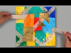 two hands are holding scissors to paint an abstract painting on a piece of paper with different colors