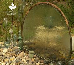 an outdoor garden with rocks and plants in the ground, along with a round mirror