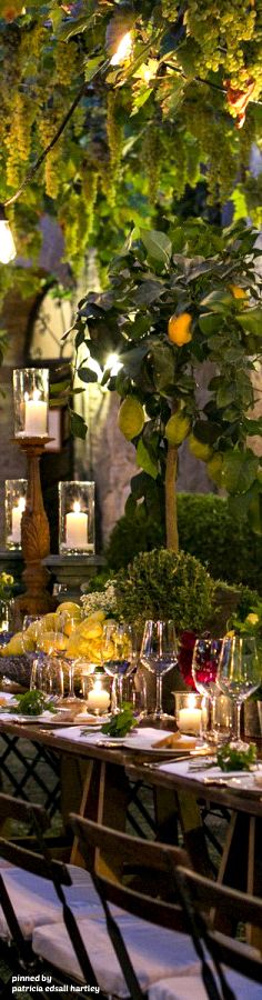 an outdoor dining area with candles and flowers on the table, surrounded by greenery