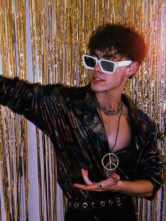 a man with sunglasses and peace sign on his arm standing in front of gold tinsel