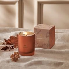 an orange candle sitting on top of a bed next to a box with leaves and flowers