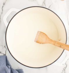 a wooden spatula in a white saucepan on a marble countertop next to a blue towel