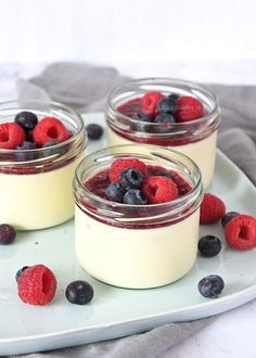 three jars filled with berries and blueberries on top of a white cloth next to some silverware