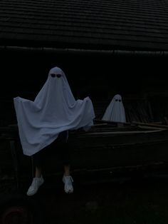 two people in white ghost costumes standing next to a boat with three ghostly figures on it