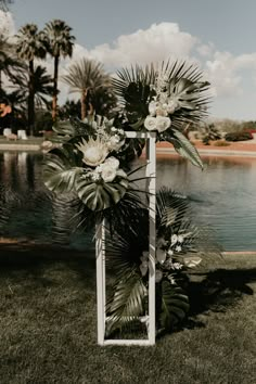 a wedding arch decorated with white flowers and greenery by the water in front of palm trees