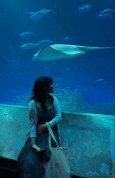 a woman standing in front of an aquarium looking at the fish swimming by her side