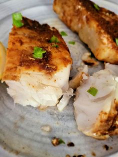 two pieces of fish on a plate with lemon wedges