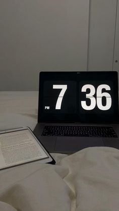 a laptop computer sitting on top of a bed next to an open book and tablet