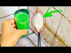 a hand holding a spoon with green liquid in it next to a cup filled with powder