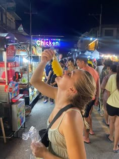 a woman is drinking from a banana at an outdoor food stand in the night time