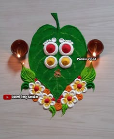 a green heart shaped decoration with two eyes and flowers on the side, surrounded by candles