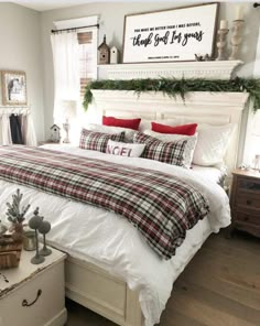 a white bed with plaid comforter and red pillows in a bedroom decorated for christmas