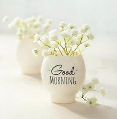 two white vases with flowers in them sitting on a table