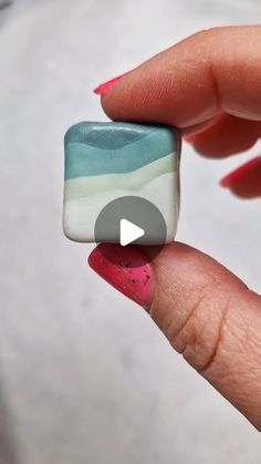 a person is holding a small square object in their left hand, with pink and blue nail polish on it