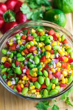 a glass bowl filled with mixed vegetables on top of a wooden table next to green peppers