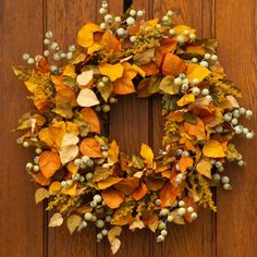 a wreath with leaves and berries hanging on a wooden door frame, ready to be used as a decoration