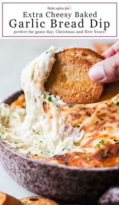 a hand holding a cracker over a bowl of garlic bread dip with cheese on top