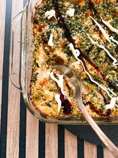 a casserole dish with spinach, cheese and sauce in it on a wooden table