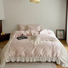 a bed with pink comforter and pillows in a white room next to a window