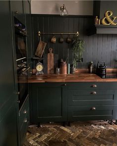 a kitchen with dark green cabinets and wooden counter tops, along with pots and pans on the wall