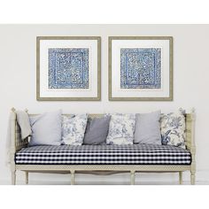 two blue and white paintings on the wall above a couch with pillows in front of it