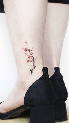 a woman's foot with a small tattoo on her left ankle and cherry blossoms on the lower leg